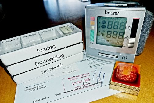 Gesundheit im Alter - Cholesterin Bild zeigt Blutdruckmanschette und Pillendosierbehälter auf einem Rezept