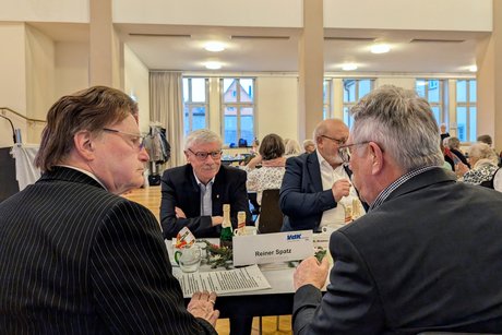 Drei Männer sitzen an einem Tisch und führen ein Gespräch. Einer von ihnen lächelt.