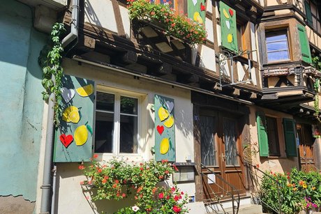 Ein sch&ouml;nes Fachwerkhaus mit bemalten Fensterl&auml;den und vielen bunten Blumen in einem typischen G&auml;sschen der Stadt.