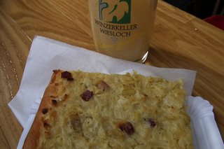 Das Bild zeigt ein Stück Zwiebelkuchen mit einem Glas neuem Wein