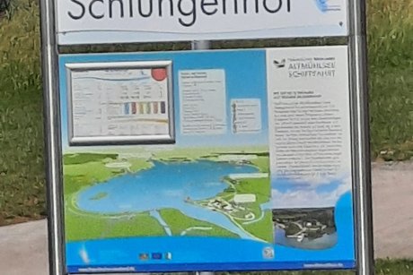 Schild mit dem Schriftzug &bdquo;Schlungenhof&ldquo; und einer darunterliegenden Karte des Altm&uuml;hlsees.