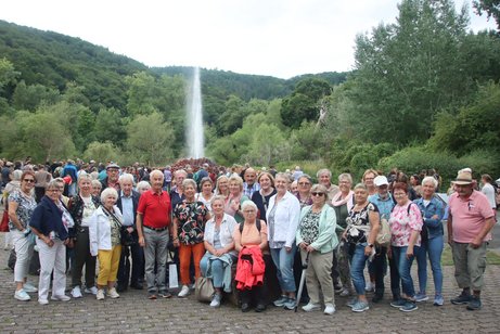 Die Ausflugsteilnehmer stehen vor der der Wasserfontäne des Geysirs in Andernach. der Himmel ist bewölkt