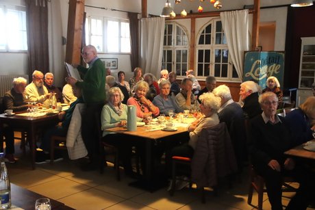 Mitglieder sitzen an Tischen beim Kaffee trinken und Kuchen essen