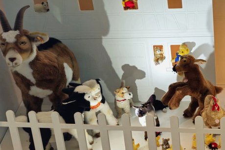 Bauernhof-Stofftiere hinter einem Holzzaun, darunter eine Ziege, ein Kälbchen, ein Hund, eine Henne und eine Katze