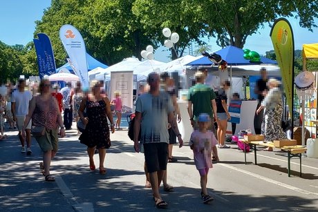 Viele Menschen laufen entlang einer Straße, an der sich auf der rechten Seite zahlreiche Informationsstände aneinanderreihen.