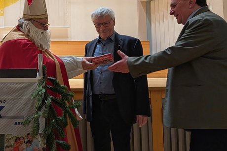 Vorweihnachtlicher Nachmittag Nikolaus überreicht einem Mann im Anzug eine Schachtel Schokolade.