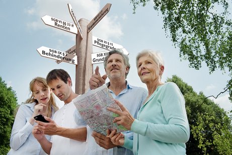 Vier Menschen mit einem ausgebreiteten Plan und einem Smartphone unter einem Wegkreuz, das in diverse Richtungen zeigt