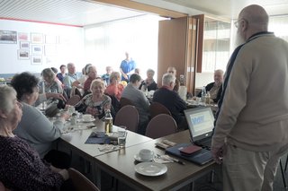 Bild zeigt zwei Tische mit Frauen u. Männern beim zuhören des Referats