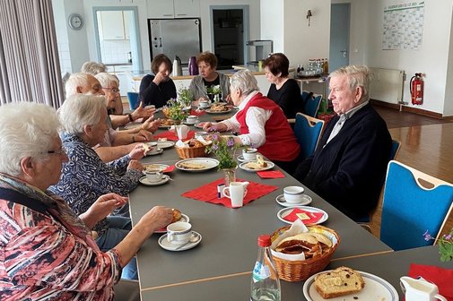 Gruppe älterer Menschen sitzt an einem Tisch mit Kaffee, Brezeln und Hefezopf.
