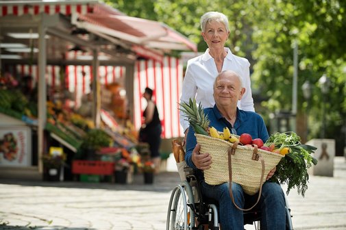 Frau hilft Mann im Rollstuhl beim Einkaufen auf dem Markt