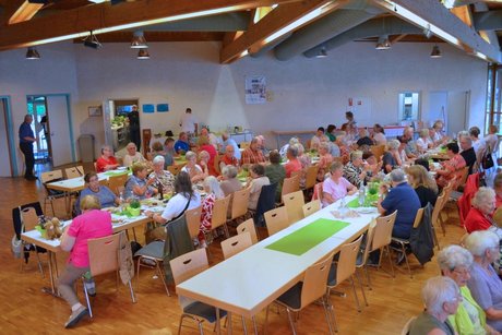Panorama des Festsaals mit mehreren Tischen, an denen Menschen sitzen und vespern.