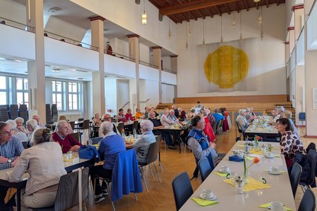 Festsaal mit mehreren Tischreihen, an denen &uuml;berwiegend &auml;ltere Menschen sitzen.