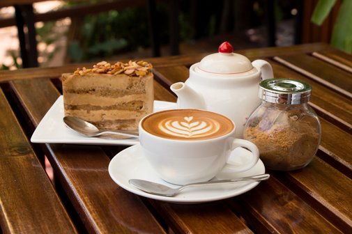 Tisch mit Kaffee in der Tasse, Teekänchen, brauner Zucker im Glas und ein Stück Sahnetorte auf einem Kuchenteller