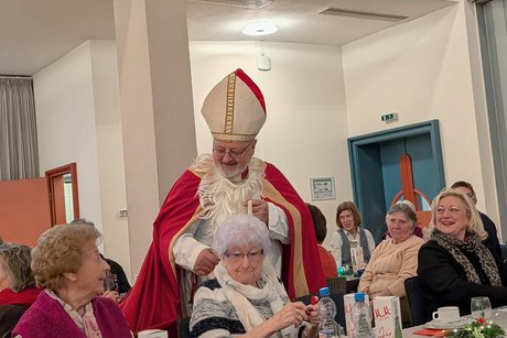 Vorweihnachtlicher Nachmittag Nikolaus mit nach unten gerutschtem Kunstbart lächelt in die Menge, die zurücklächelt.