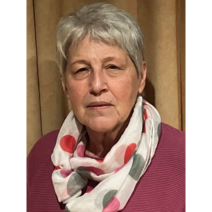 Dame mit silbergrauen Haaren tr&auml;gt brombeerfarbenen Pullover und wei&szlig;en Schal mit bunten Punkten.