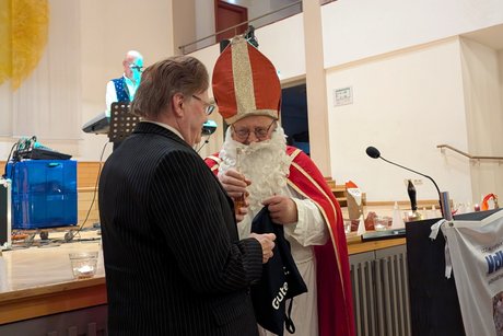 Ein Mann im Nikolauskostüm überreicht einem Mann im festlichen Anzug ein Präsent.