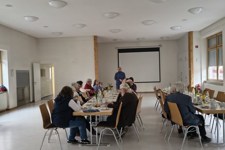 an zwei eingedeckten Kaffeetafeln sitzen einige Personen
