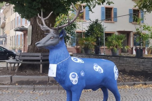 Die Schönauer Wappentier-Skulptur, Hirsch Fridu von der Linde, neben der Gerichtslinde in dunkelblau bemalt mit weißen Flecken und versehen mit VdK-Aufklebern
