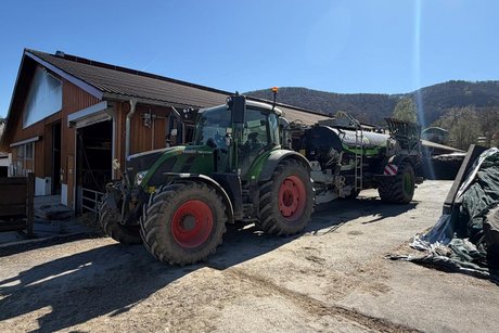 Auf dem Sulzburghof. Ein Traktor mit G&uuml;llewagen steht vor dem Kuhstall