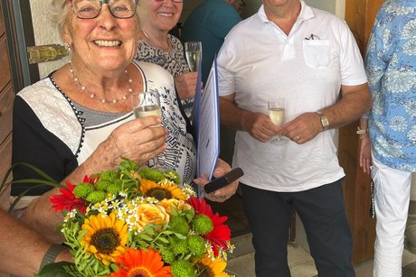 Marlies strahlt mit einem bunten Blumenstrau&szlig;, einem Glas Sekt und der Ehrenmedaille, auch der Kreisvorsitzende und die Frauenbeauftragte strahlen.