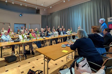 Blick von vorne in den Saal auf die abstimmenden OV-Vertreter; schräg im Vordergrund ist teilweise der geschäftsführende Vorstand zu sehen.