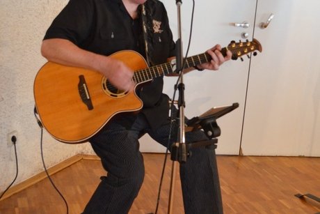 Ein Mann, der sitzend Gitarre spielt und dabei singt.