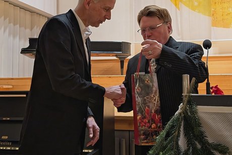 Vorweihnachtlicher Nachmittag Mann im Anzug überreicht dem Dirigenten im Anzug eine Geschenktüte mit einer Weinflasche.