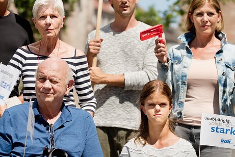Gruppe von Menschen verschiedenen Geschlechts und Alters, mit und ohne Behinderung, demonstrieren. Auf einer Demopappe steht "Pflege darf nicht arm machen"