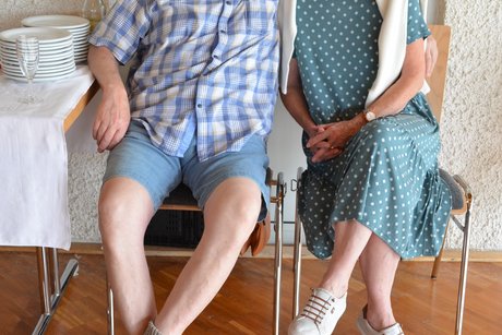 Mann mit Bart und Frau, die nebeneinander auf Stühlen sitzen.