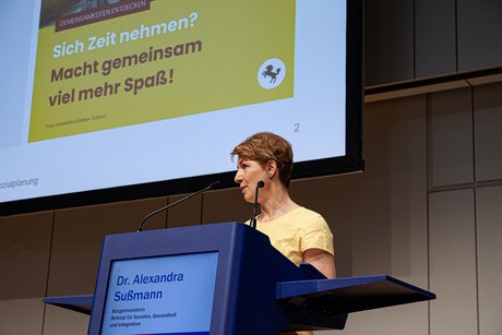 Dr. Alexandra Süßmann, Bürgermeisterin Referat für Soziales, Gesundheit und Integration steht am Pult und am Mikrofon, hinter ihr auf der Leinwand ein Bild