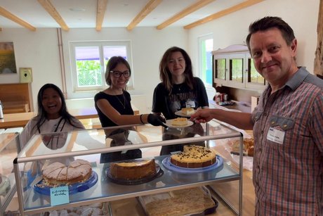 Das Photo zeigt drei Mädchen, die lachend hinter der Kuchentheke und einem VdK Vorstandsmitglied gerade einen leckeren Kuchen über die Theke reichen.