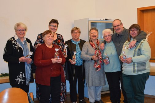 Gruppenbild mit sieben Frauen unterschiedlichen Alters und einem Mann, die nebeneinander stehen und kleine Geschenkt&uuml;ten in den H&auml;nden halten.