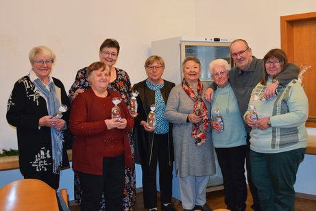 Gruppenbild mit sieben Frauen unterschiedlichen Alters und einem Mann, die nebeneinander stehen und kleine Geschenkt&uuml;ten in den H&auml;nden halten.