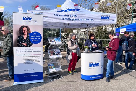 Der VdK am Infostand vertreten unterm Faltzeltdach mit Rollup des VdK und Brosch&uuml;renst&auml;nder und VdK-Werbetheke mit einer Besucherin