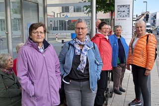 Teilnehmer warten an der Bushaltestelle auf den Reisebus