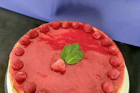 Eine wundersch&ouml;ne Himbeertorte mit rotem Decorspiegel und ringsherum frische frische Himbeeren.