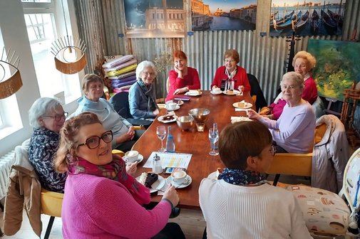 Neun Frauen sitzen um einen Tisch mit Kaffee und Kuchen.