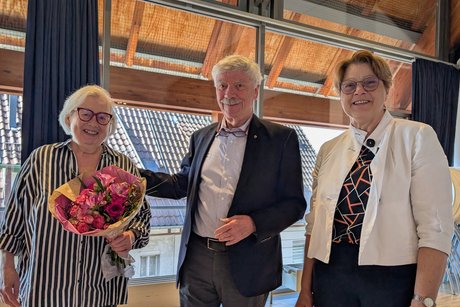 Gruppenfoto: Links eine Dame in einer schwarz-wei&szlig; l&auml;ngsgestreiften Bluse, die einen Blumenstrau&szlig; h&auml;lt. Daneben ein Herr im Anzug, der seine Hand auf ihre Schulter gelegt hat. Rechts steht eine l&auml;chelnde Dame in einem modischen Blazer.