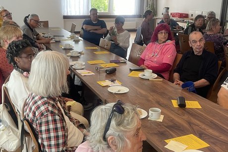 Eine Gruppe von &auml;lteren Menschen sitzt um einen Holztisch in einem Raum.