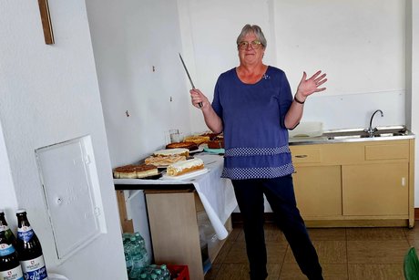 Regina unsere Kassiererin fuchtelt fröhlich mit dem Kuchenmesser vor der Kuchentheke.