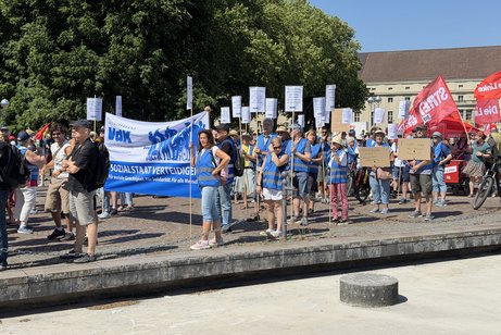 Demonstrationszug: Menschen mit Banner und Plakaten laufen durch die Innenstadt von Karlsruhe, die Sonne scheint.