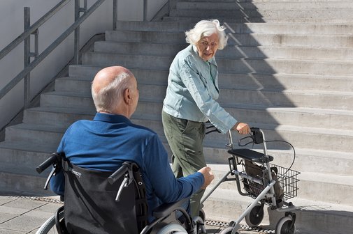 Ein Rollstuhlfahrer und eine Dame mit Rollator vor einer Treppe