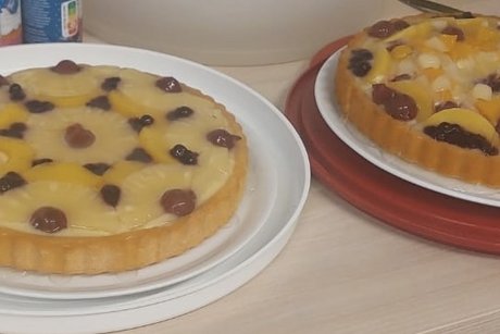 Zwei vollständige Kuchen stehen nebeneinander. Sie sind mit verschiedenen Obstsorten belegt.