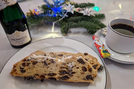 Teller mit zwei Scheiben Christstollen, daneben ein Piccolo und eine Tasse Kaffee. Vor dem Teller dekoratives Tannenreisig.