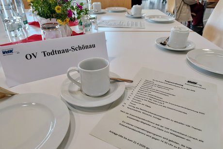 Tisch mit schmucken Blumen, gedeckt mit Kaffee- und Kuchengeschirr, Namensschild des Ortsverbands und Tagesordnung