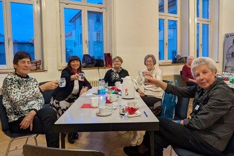Fünf ältere Frauen an einem Tisch, die ihre Gläser in Richtung Kamera zum Prosit halten. Die meisten von ihnen lächeln.
