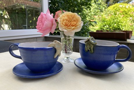 Zwei Kaffeetassen auf dem Tisch, dazwischen eine kleine Vase mit Rosen