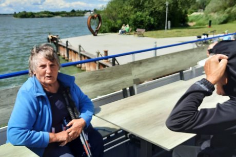 Eine Frau sitzt auf dem offenen Oberdeck und blickt in die Kamera, im Hintergrund der See.