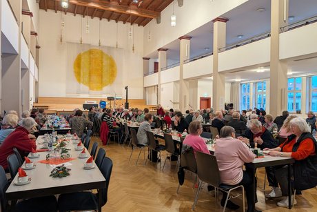 Festsaal mit Tischreihen, an denen zahlreiche Gäste sitzen.