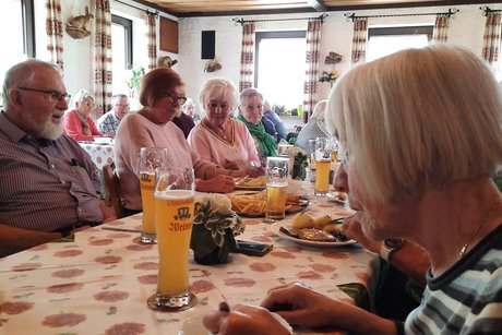Tischreihe, an der mehrere &auml;ltere Menschen gemeinsam zu Mittag essen und sich angeregt unterhalten.